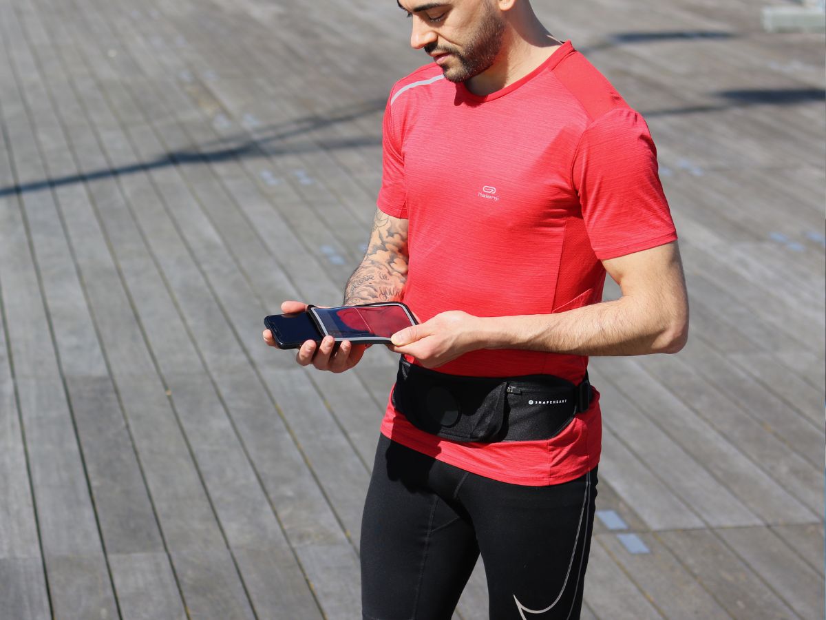 Corredor con chaqueta impermeable corriendo bajo la lluvia con un brazalete resistente al agua visible en el brazo, ilustrando la protección de los dispositivos electrónicos durante la carrera.
